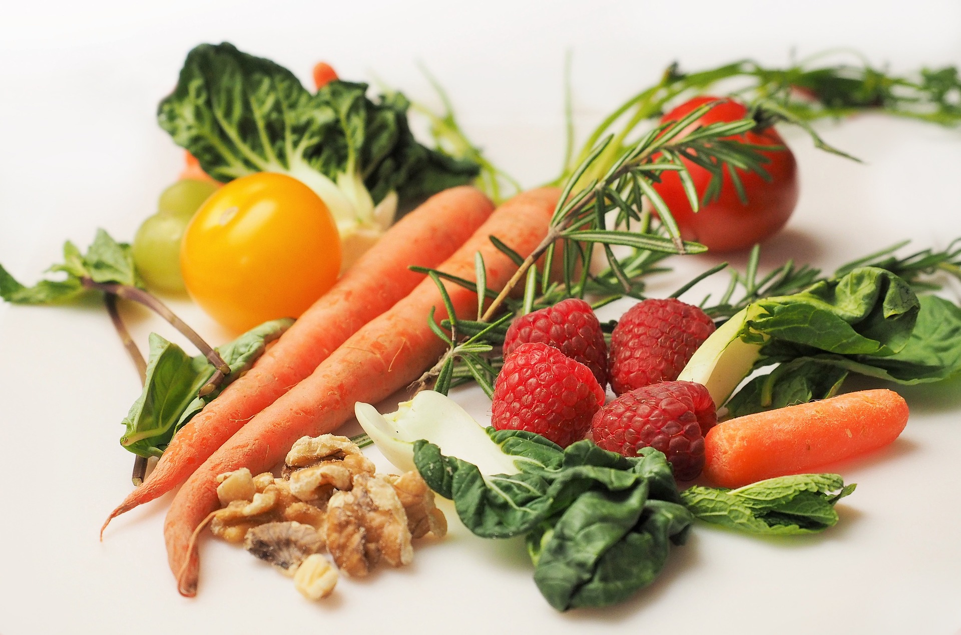Assortment of healthy foods, including walnuts, raspberries, carrots, red and yellow peppers, tomatoes, and greens